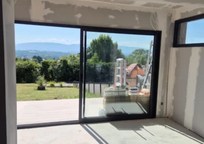 Baie vitrée de l’extension offrant une vue dégagée sur le jardin et les montagnes